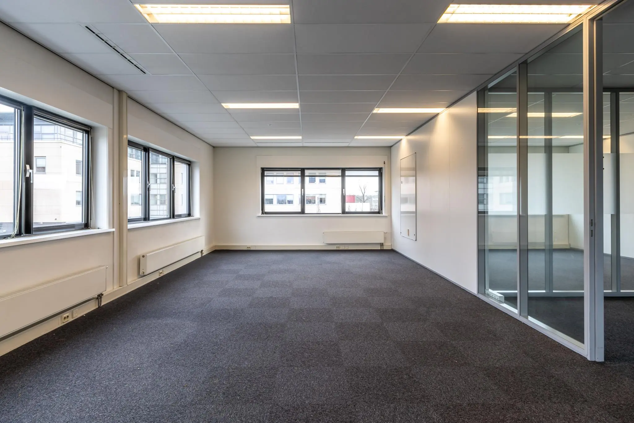 Lichte, lege kantoorruimte aan de Lage Biezenweg met grote ramen en glazen scheidingswand.